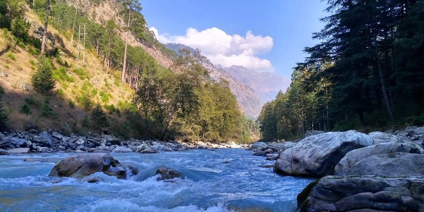 Scenic view of Kasol village with the Parvati River flowing between pine forests and hills, showing snowfall in Kasol.