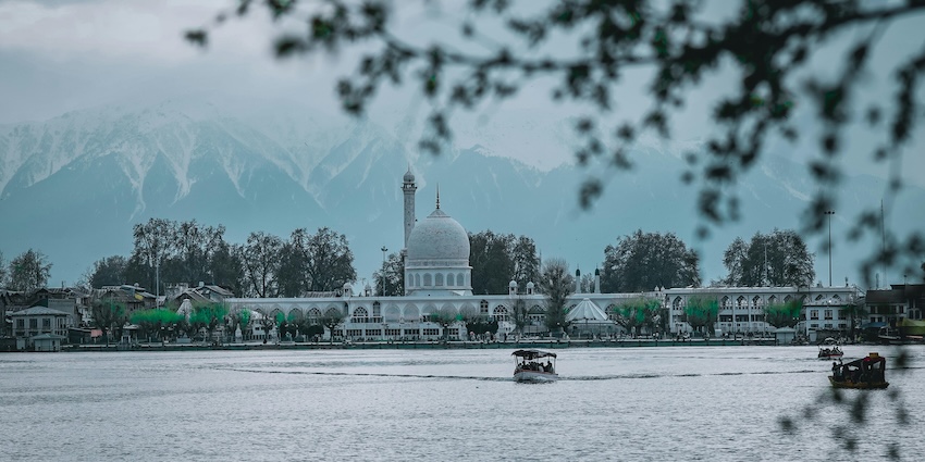 Hazratbal Shrine at a distance beyond a large waterbody and Zabarwan range, showing snowfall in Srinagar.
