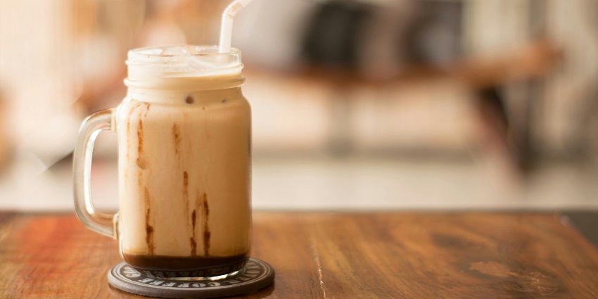 Cold coffee served at Black Coffee Cafe on a wooden table with a straw and a frothy top.
