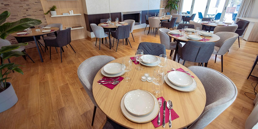 Elegant dining room with round wooden tables, grey chairs, and bright natural lighting at Blue Orchid Restaurant.
