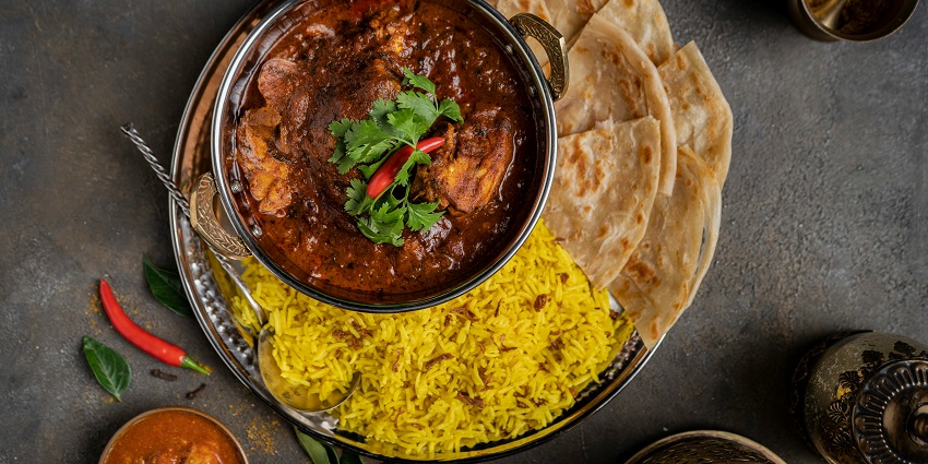 A bowl of Indian curry served with rice and naan at Bombay Brasserie.
