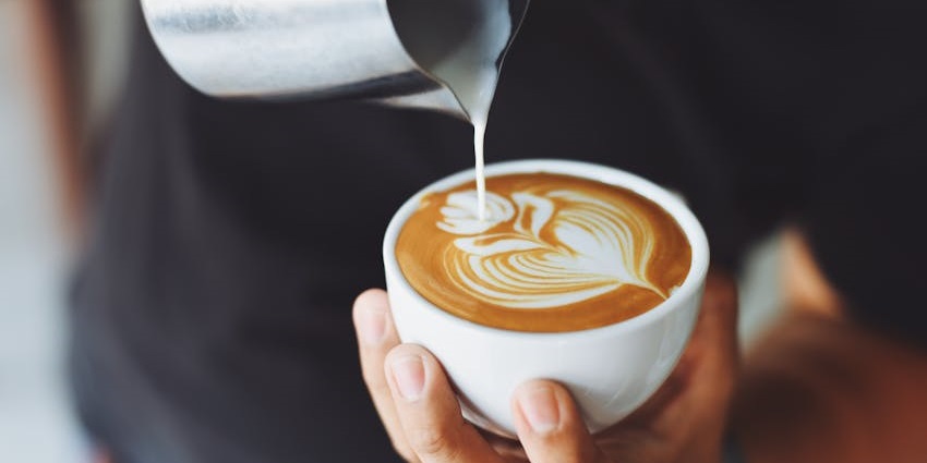 Close-up of milk being poured to create detailed latte art in a white coffee cup.
