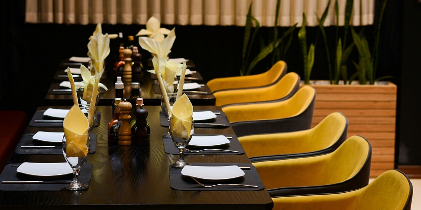 Café B-You interior featuring a long table with yellow chairs and black tablecloths.

