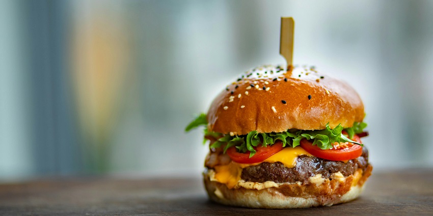 A burger served at Café Coffee Day with fresh lettuce and cheese on a wooden plate.

