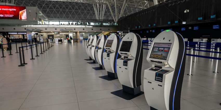 Row of self-service check-in kiosks inside a spacious modern airport terminal building