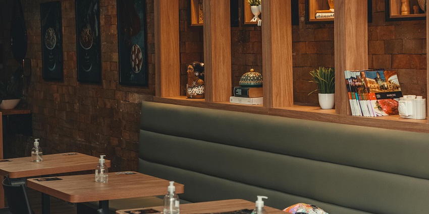 Restaurant interior with brick wall, wooden shelves, and neatly set wooden tables.
