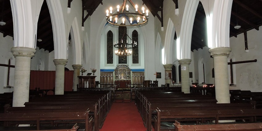 Interior view of Christ Church Kasauli with wooden pews, arched pillars, and chandeliers.