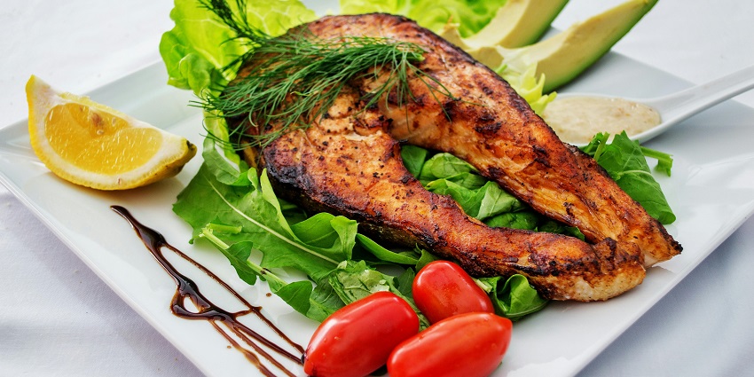 Grilled salmon steak on fresh greens with cherry tomatoes, avocado and lemon wedge.
