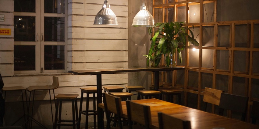Cosy café corner at Dream Cafe with wooden tables, pendant lights, and a green plant accent, one of the best restaurants in Silchar.
