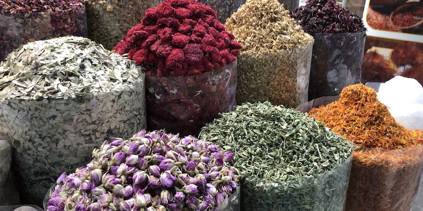 Mounds or piles of different colored spices arranged in baskets, sacks, or bins.