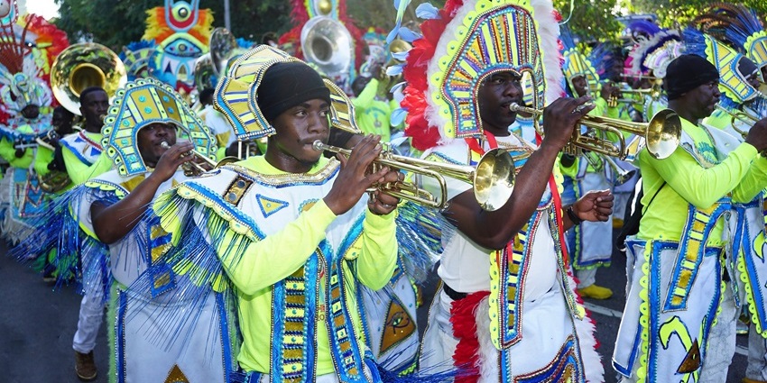 Image of participants in colorful, elaborate costumes playing trumpets and saxophones.