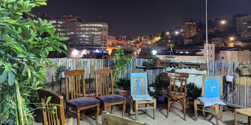 Rooftop café in downtown Amman at night with wooden chairs and city lights, showing snowfall in Kasol.