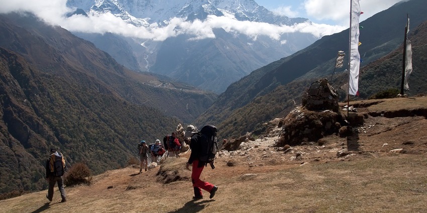 Trekkers walking along a mountain trail with snow-covered Himalayan peaks , showing snowfall in Kasol.