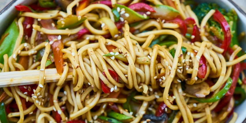A plate of noodles with veggies, and chopsticks served at FLAVOUR Restaurant.
