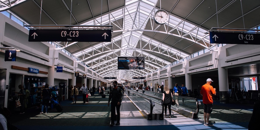 Travellers walking through a bright airport terminal with moving walkways and gate signs, representing airports in Tripura.