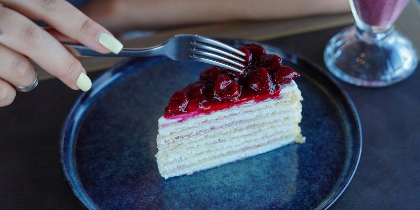 Slice of layered cake with cherry topping on a blue plate, served with milkshake.