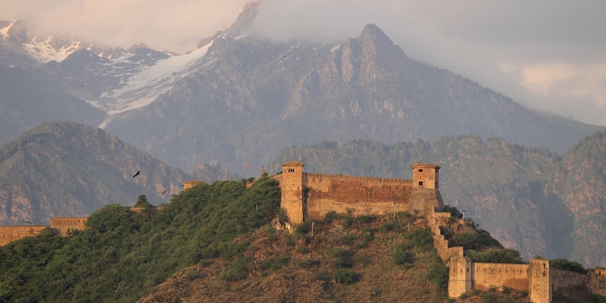 Hari Parbat Fort’s old structure on a hill covered in greenery and huge mountains in background