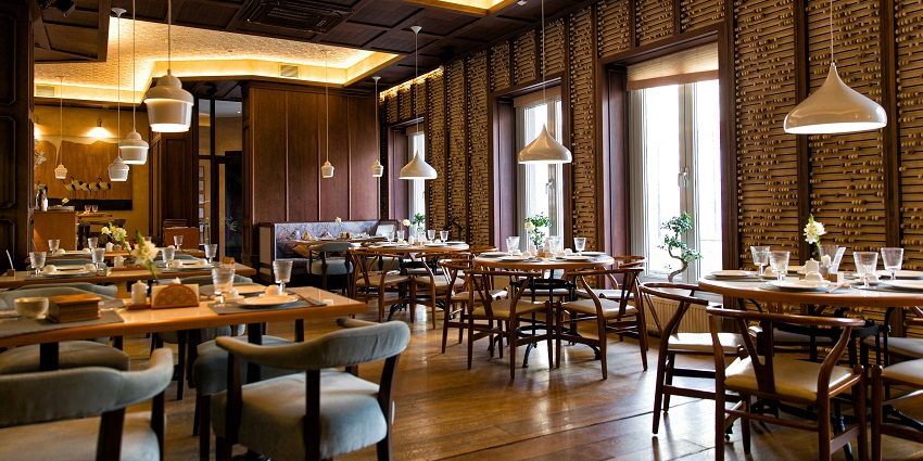 Interior of Hotel Gulmohar Grand Restaurant with table, chairs, and hanging lights creating a cosy atmosphere.
