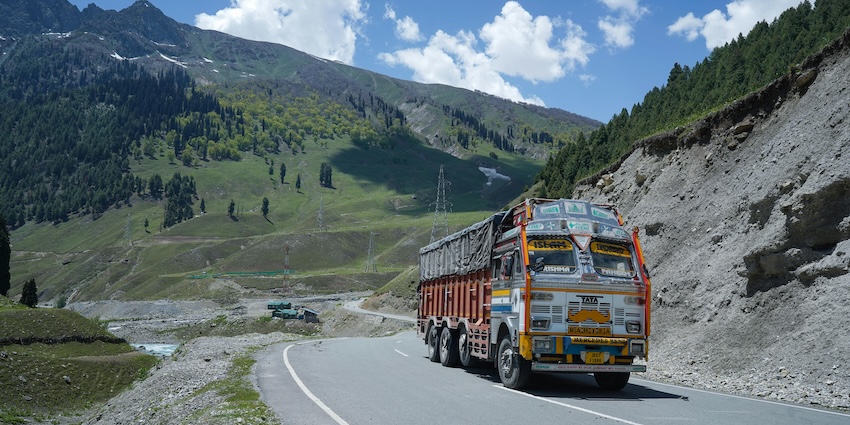 A truck riding on the Kashmir highway and mountains covered in greenery under blue sky