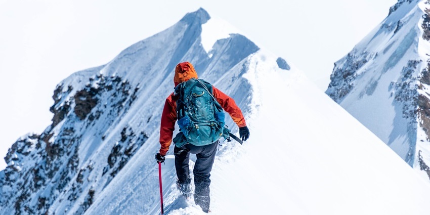 Mountain climber ascending a steep, narrow snow ridge amid snowy alpine peak