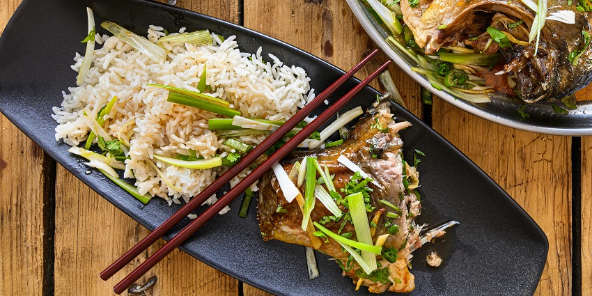 Steamed rice with scallions served beside braised fish topped with herbs and soy glaze.
