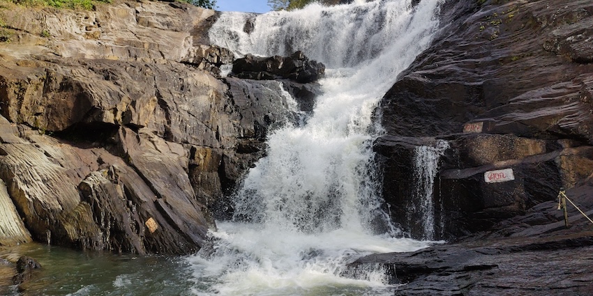 Water cascading down jagged, dark brown rocks into a pool, one of the best among Tripura waterfalls.