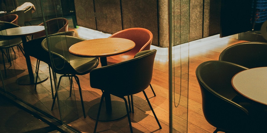 Small round tables with modern chairs set near a counter in a warmly lit restaurant space.
