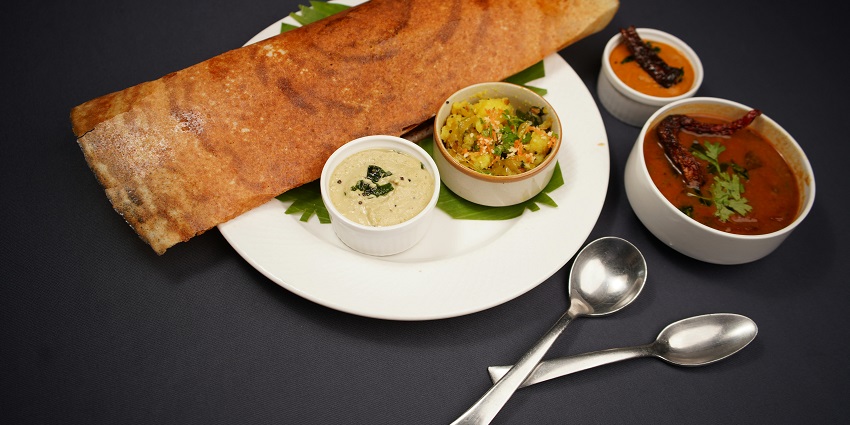 Dosa served with chutney and sambar on a white plate at Kanhaa restaurant.

