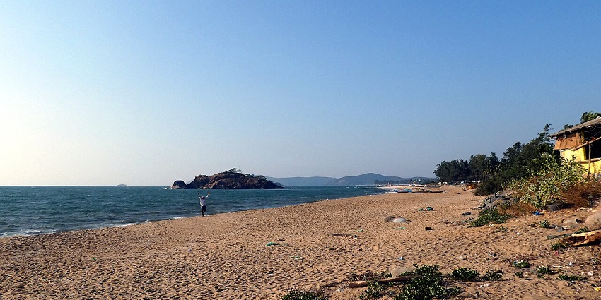 A person on a wide sandy beach with a small island in the distance perfect for road trips from Goa.