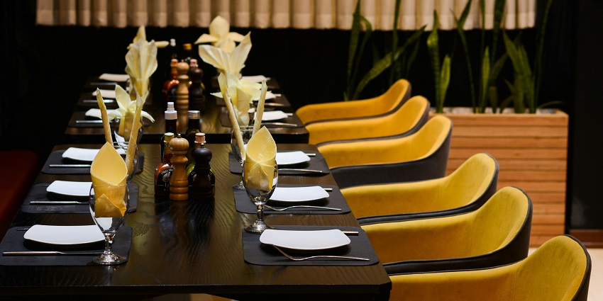 Interior of Khorikaa featuring a long table with yellow chairs and black tablecloths.