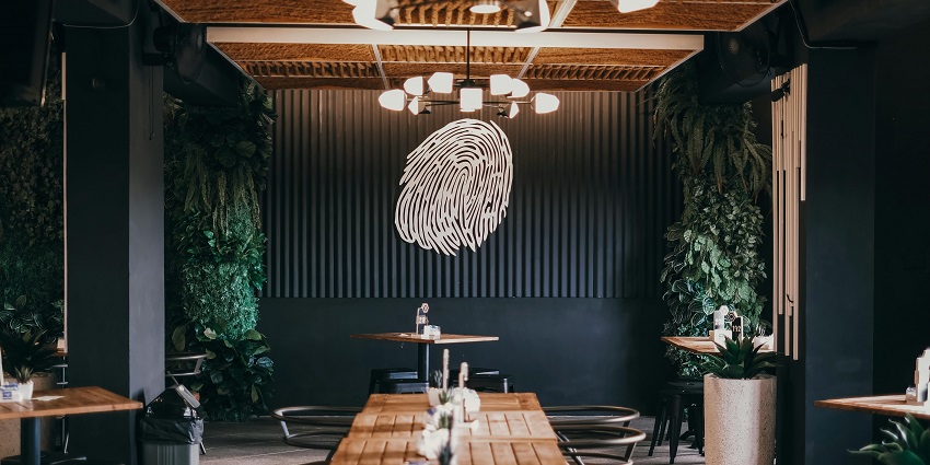 Modern café interior with wooden tables, plant décor, and a wall art fingerprint design.