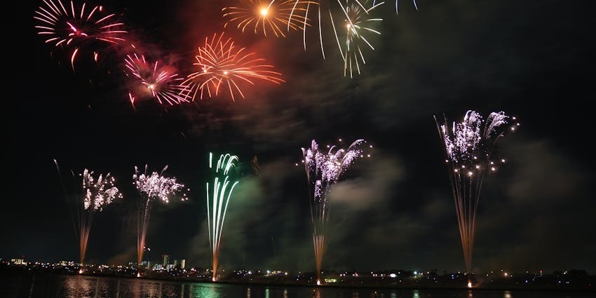 Vibrant fireworks burst above Pondicherry skyline, reflecting on the water for the New Year in Tamil Nadu.