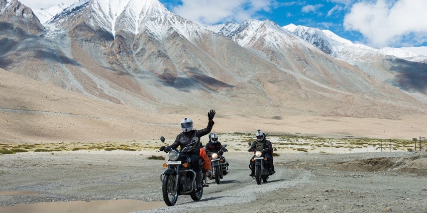 A stunning view of riders riding their bikes near Pangong Lake with mountains at the back.
