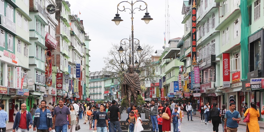 Busy M.G. Marg in Gangtok with people walking, colourful buildings, and a Gandhi statue at the centre