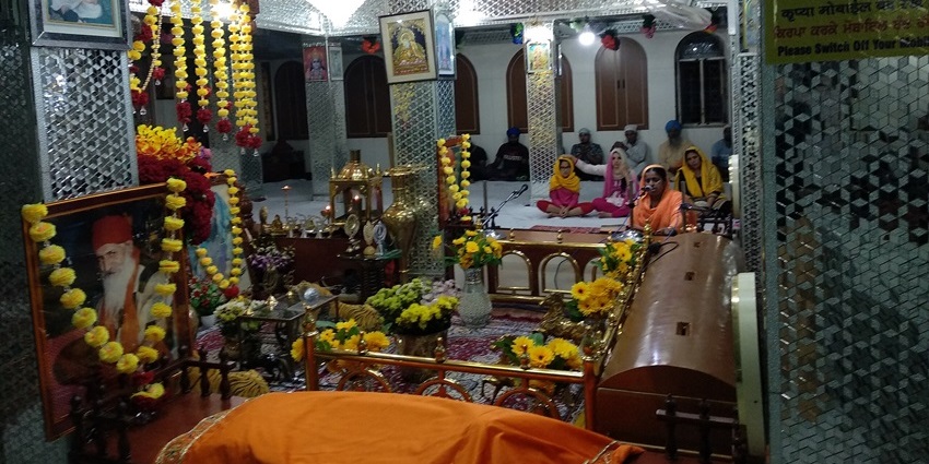 Interior of Manikaran Sahib Gurudwara decorated with lights, chandeliers, and floral garlands, showing snowfall in Kasol.
