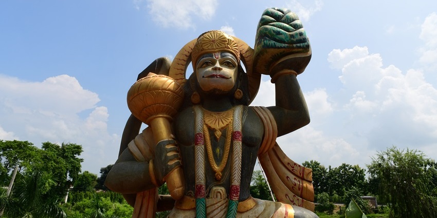 Large statue of Lord Hanuman holding a mace and mountain, set against a clear blue sky, showing snowfall in Kasauli.
