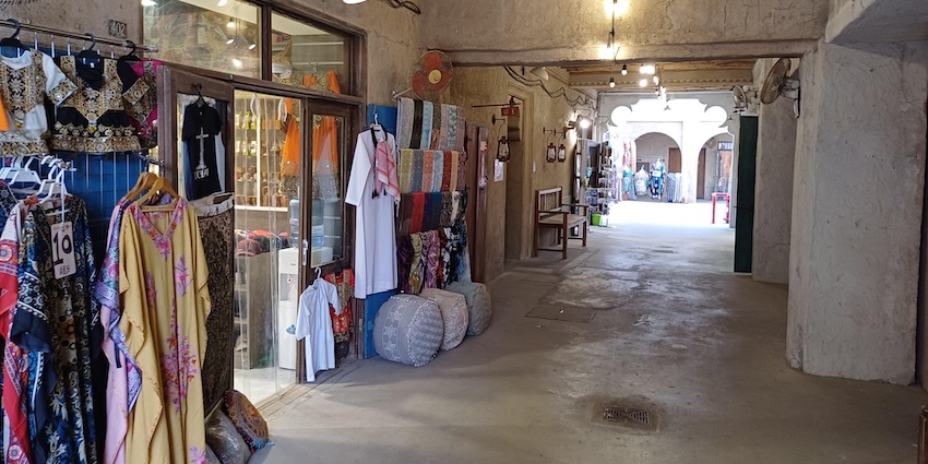 A brightly lit, covered alleyway lined with shops displaying a variety of colourful textiles, garments, one of the best markets in Dubai.