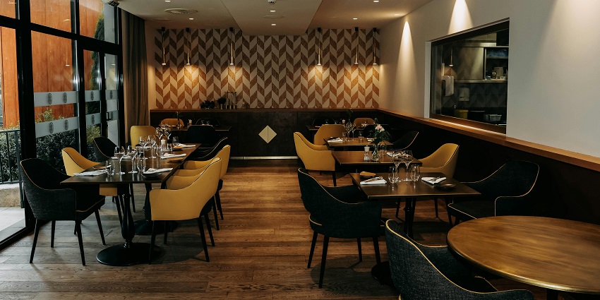 Modern restaurant interior with patterned wall, wooden flooring, and neatly set tables, one of the top restaurants in Jorhat.
