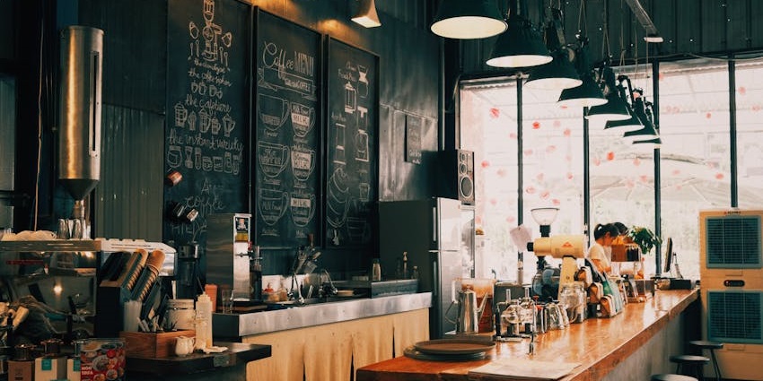 Cosy café interior with chalkboard menus, wooden counter seating, and warm hanging lights.