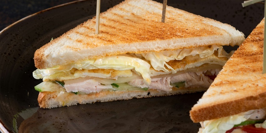 Chicken sandwich served at Oasis Cafe on a wooden plate with fries – cafes in MG Marg Gangtok.