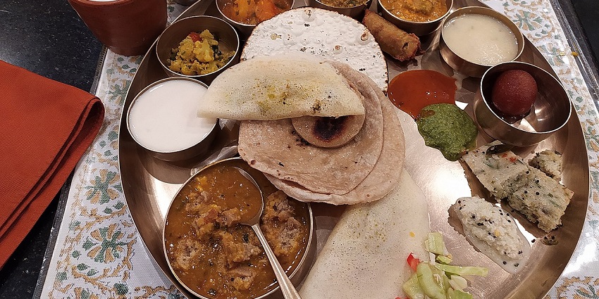 A large metal thali platter with multiple bowls of food, flatbreads, and drinks.