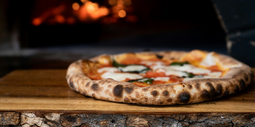Wood-fired pizza topped with cheese and herbs served hot on a wooden plate.