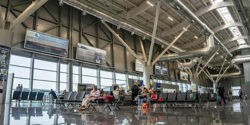 Passengers sitting and waiting inside a modern airport departure lounge with high ceiling in airports in Tripura.