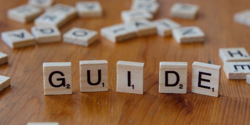 Wooden Scrabble tiles spelling 'guide' on a wooden surface with scattered letters.