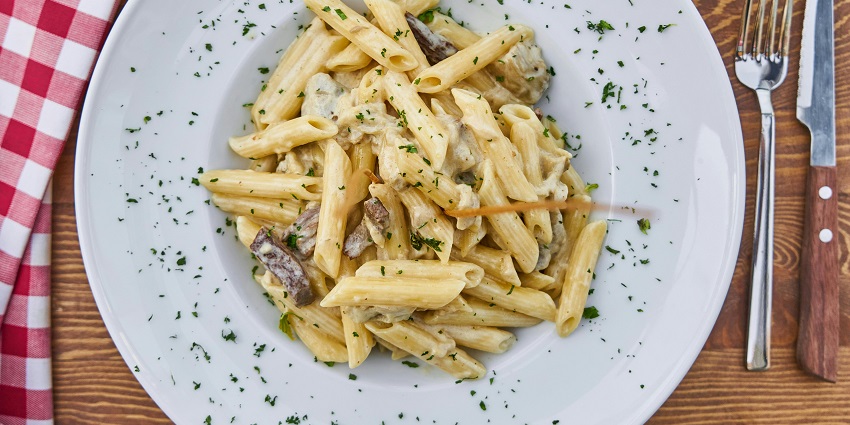 Creamy penne pasta served with mushrooms, garnished with herbs on a white plate.
