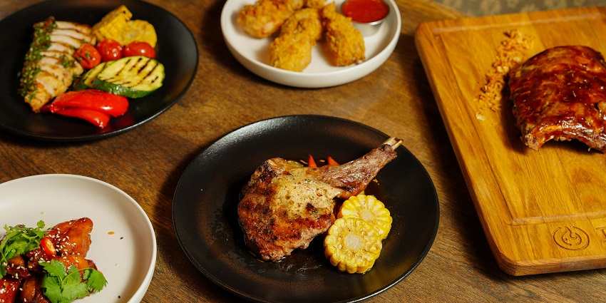 Assorted dishes with grilled meat, fried chicken, ribs, and vegetables served on plates.