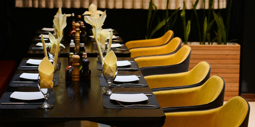 Interior of Rhododendron Restaurant with long table, yellow chairs, black cloths.