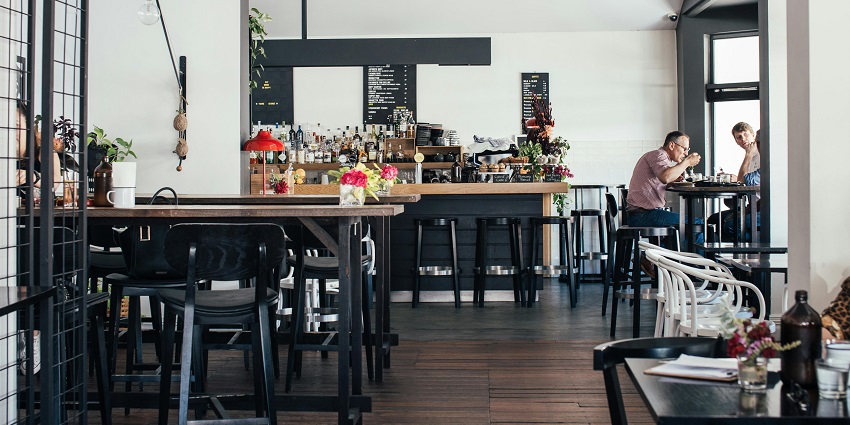 Modern café interior with wooden tables, bar counter, and two people dining, one of the iconic restaurants in Aizawl.