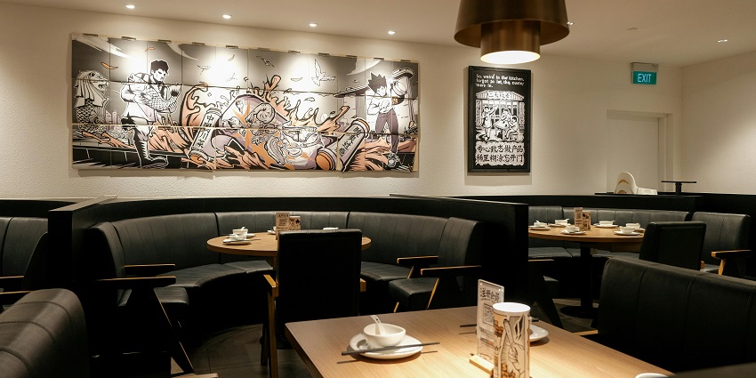 Restaurant with round wooden tables, dark seating, and wall art under warm pendant light.
