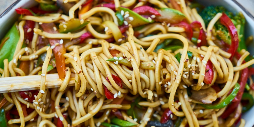 Bowl of stir-fried noodles with peppers and sesame, served with chopsticks at Saffron Restaurant, one of the best restaurants in Tezpur.

